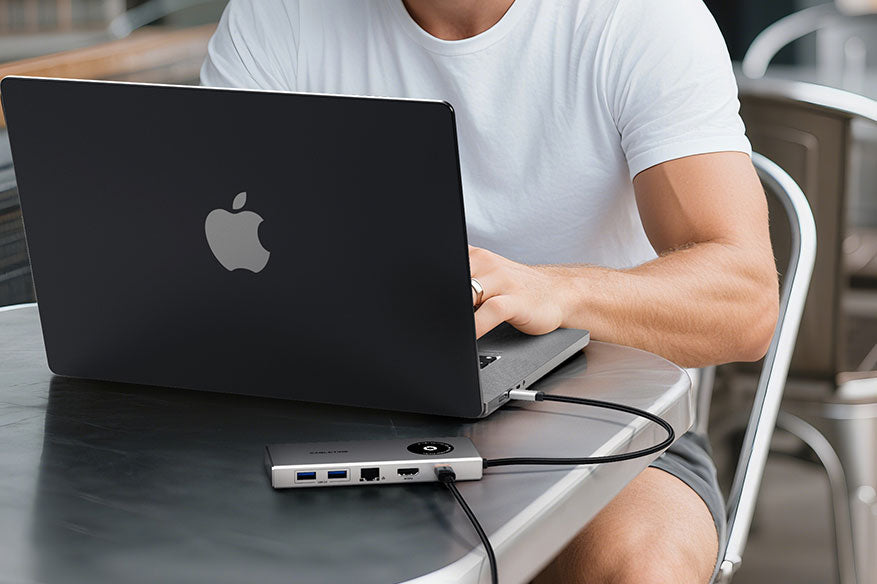 Man using a MacBook connected to Cabletime USB-C dock at a café, showing portable productivity setup.